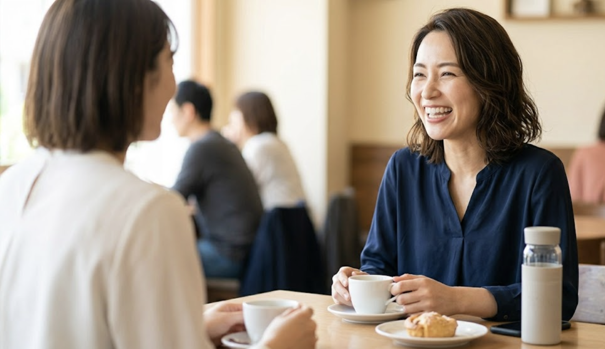 カフェで友人と談笑する日本人女性。インビザライン（透明なマウスピース）を装着しているが目立たず、自然な笑顔を見せている。