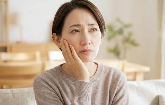 ぼんやりと口元の不調を案じる日本人女性
