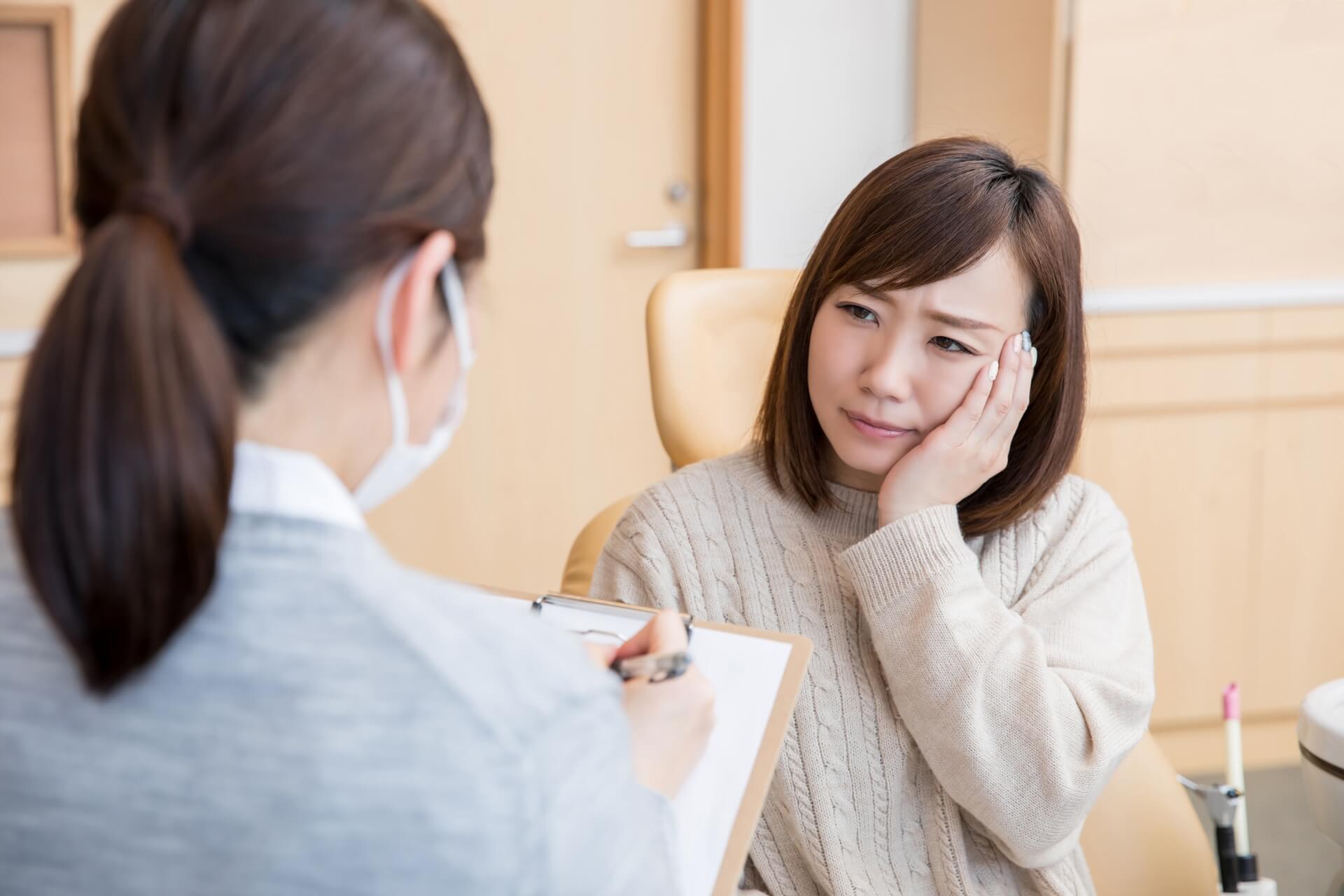 カルテを持つスタッフの前で、お口の中の変化による痛みに困った表情を見せる女性の様子