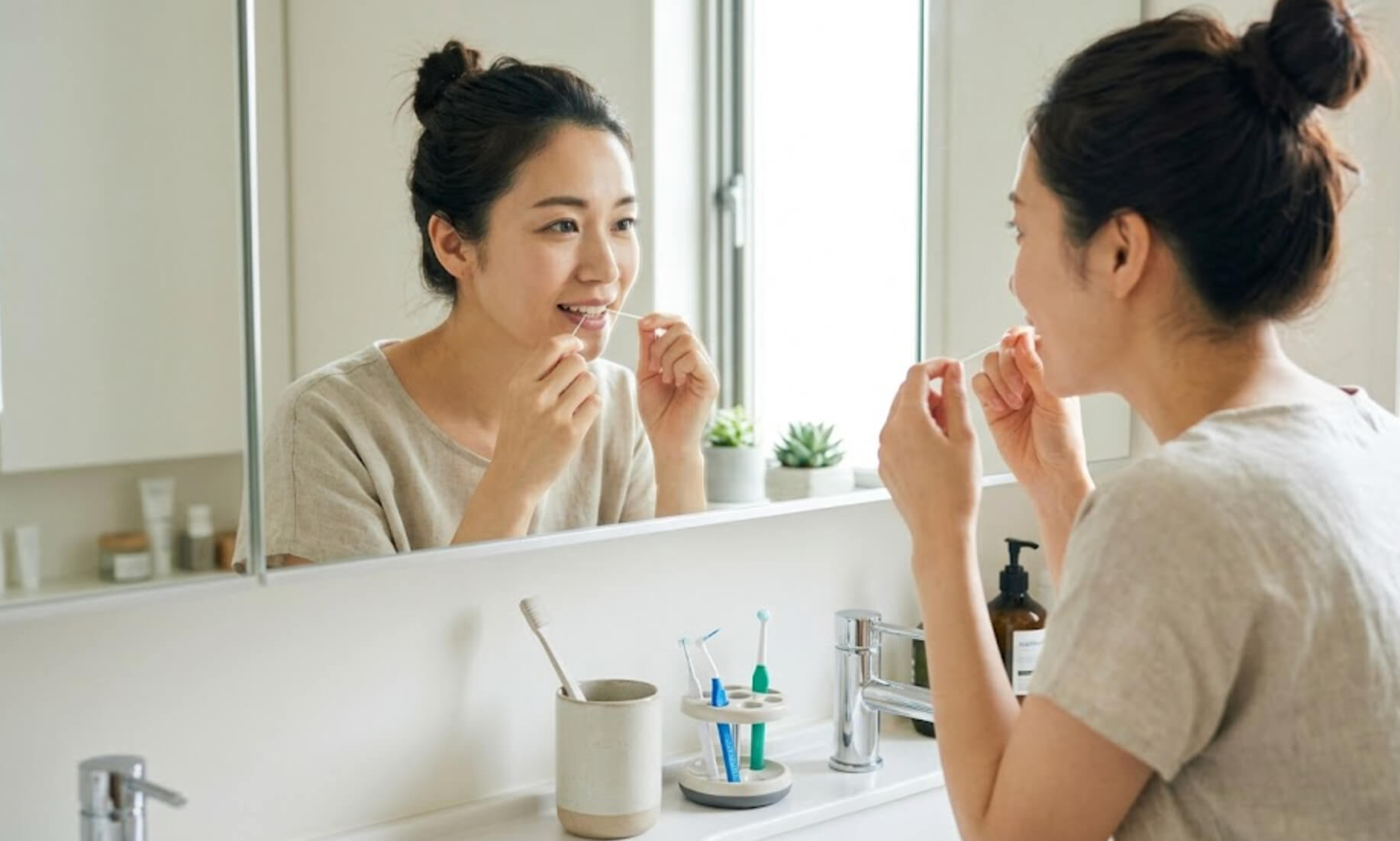 洗面所の鏡の前でフロスをする日本人女性の様子